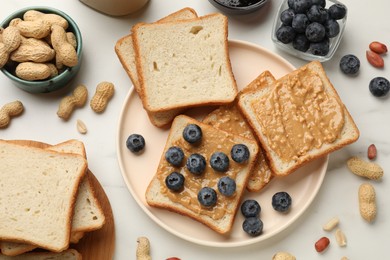 Photo of Delicious toasts with peanut butter, blueberries and nuts on white marble table, flat lay