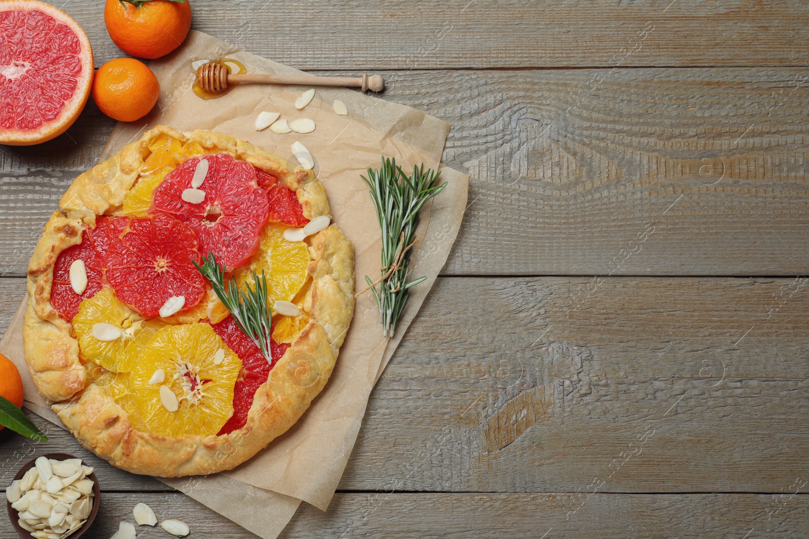 Photo of Delicious galette with citrus fruits, almond flakes and rosemary on wooden table, flat lay. Space for text