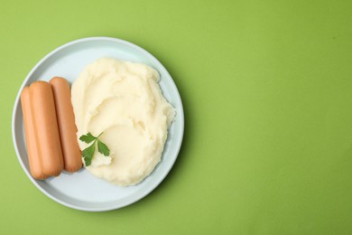 Delicious boiled sausages, mashed potato and parsley on green background, top view. Space for text