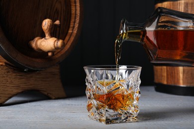 Photo of Pouring whiskey into glass from bottle and wooden barrels on table. Space for text