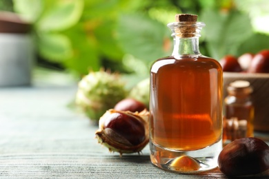 Chestnuts and bottle of essential oil on blue wooden table. Space for text