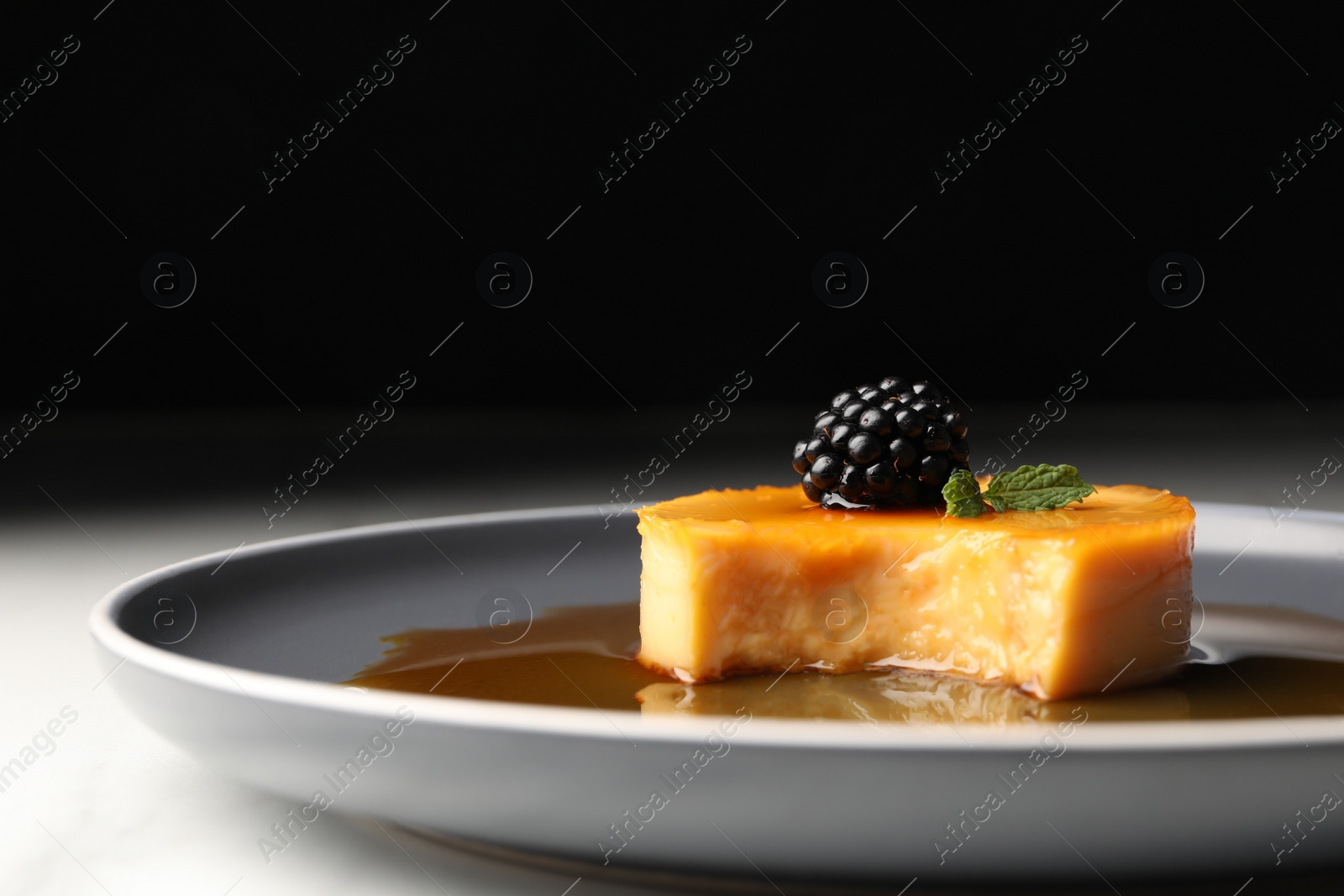 Photo of Delicious pudding with caramel and blackberry on plate, closeup