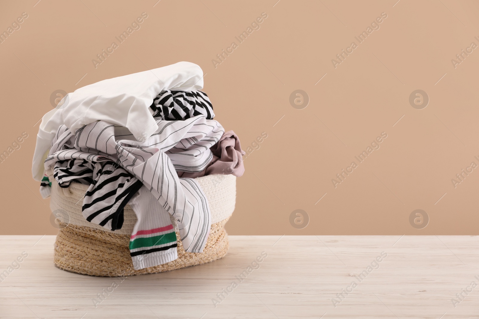 Photo of Wicker laundry basket with clothes near beige wall. Space for text