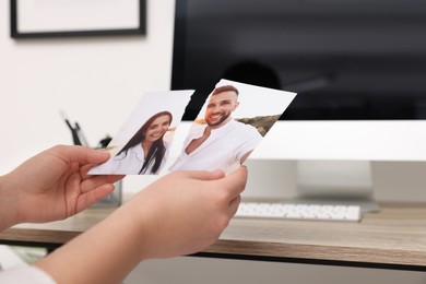 Photo of Woman holding torn photo at wooden table indoors, closeup. Divorce concept