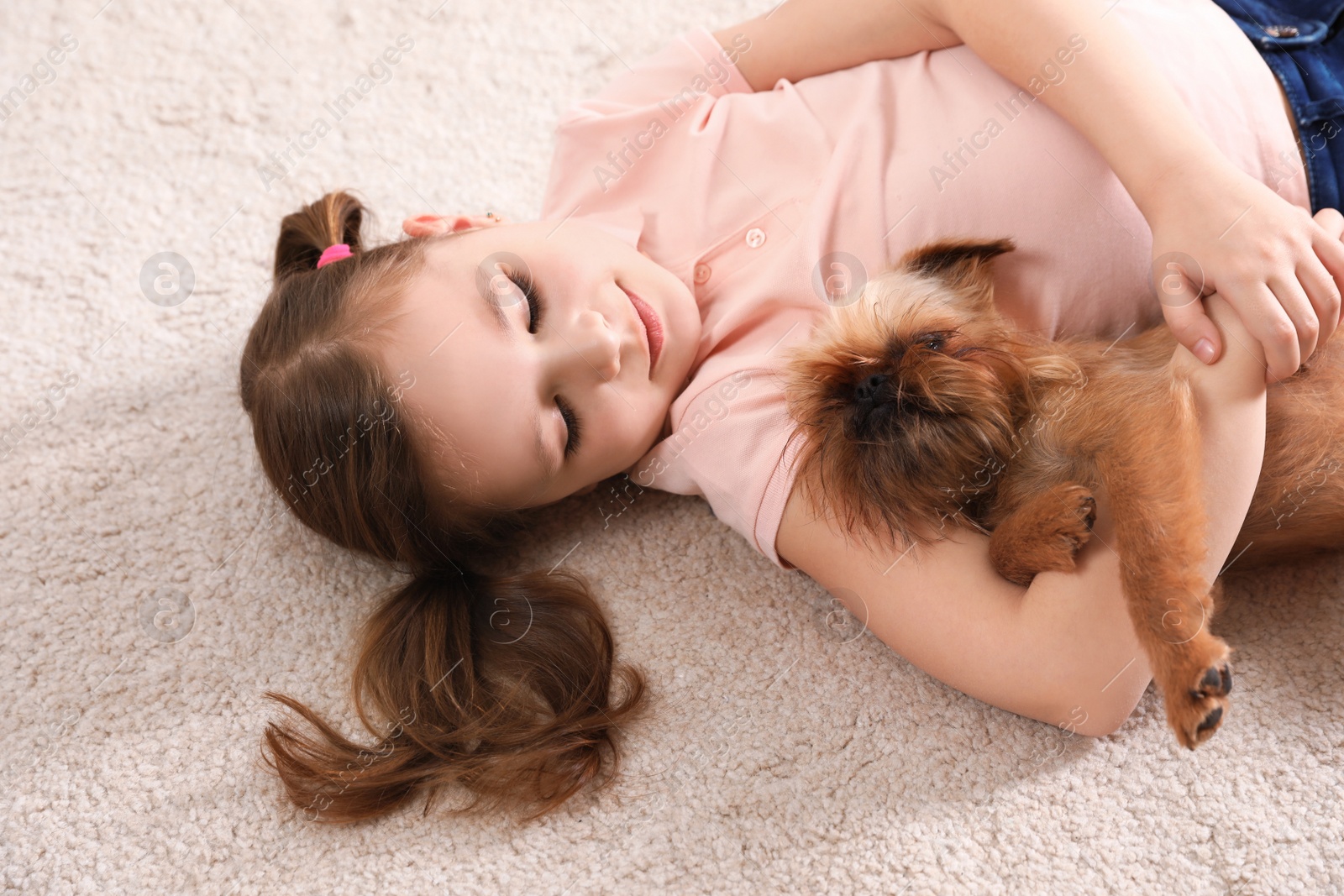 Photo of Portrait of cute girl with funny Brussels Griffon dog lying on carpet. Loyal friends