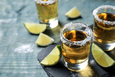 Photo of Mexican Tequila shots, lime slices and salt on blue wooden table