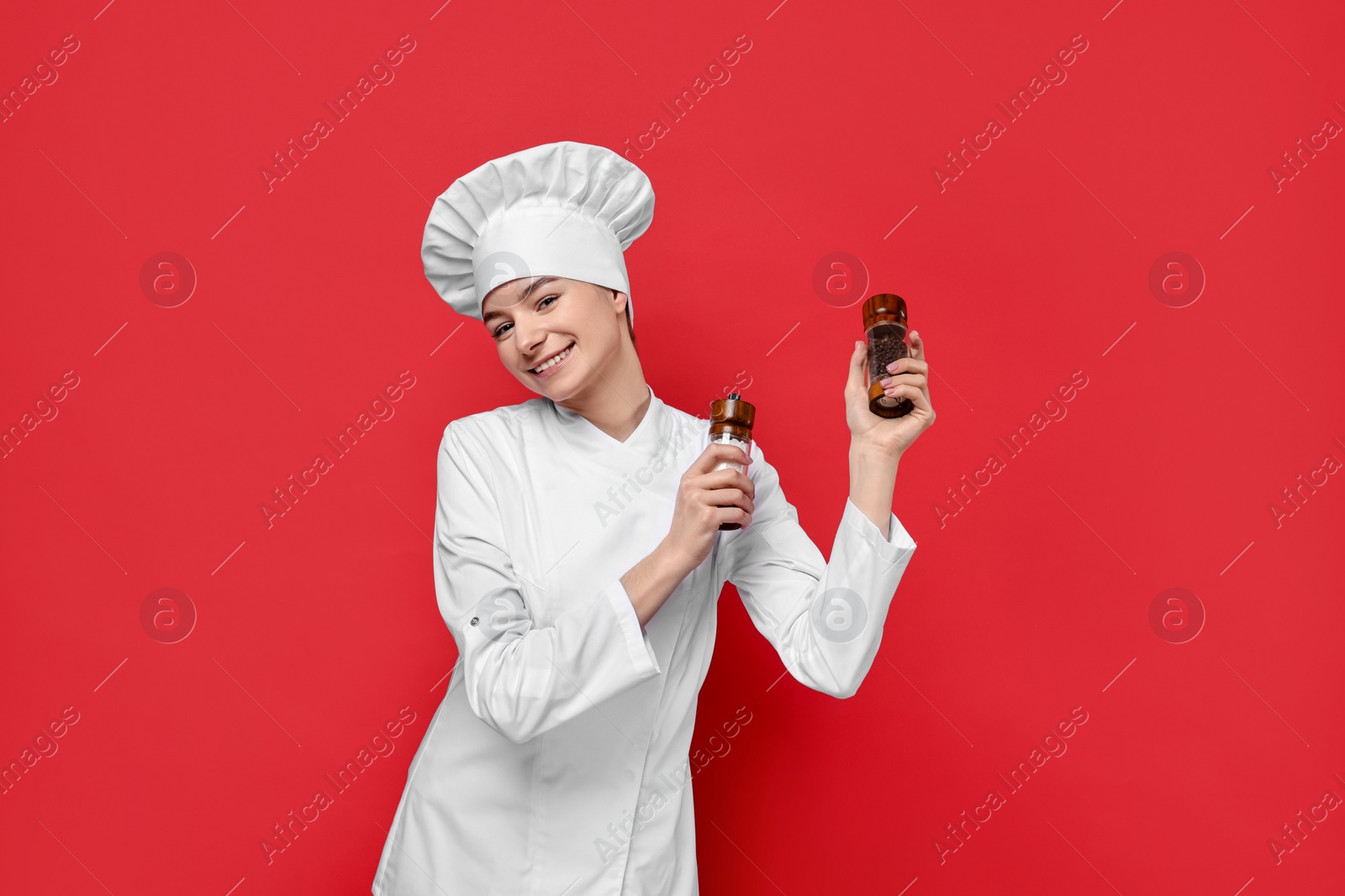 Photo of Professional chef holding salt and pepper shakers on red background