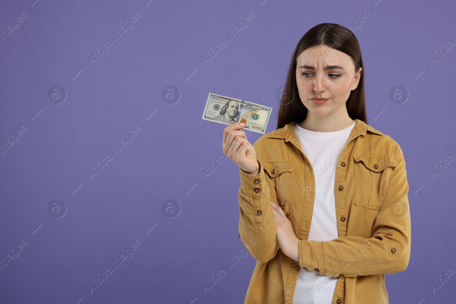 Photo of Sad woman with dollar banknote on purple background, space for text