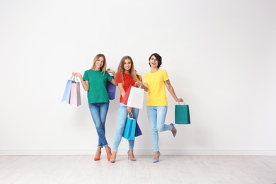 Group of young women with shopping bags near light wall