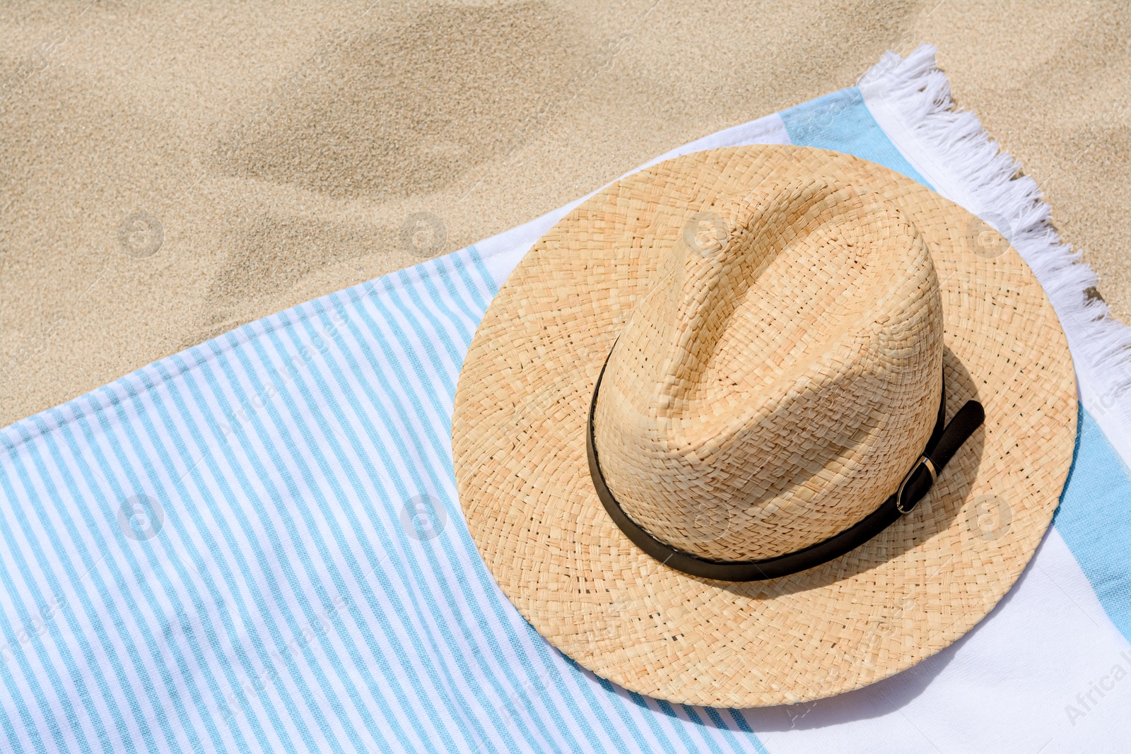 Photo of Beach towel with straw hat on sand. Space for text