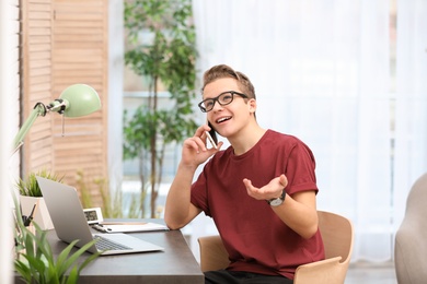 Photo of Handsome teenage boy talking on phone at table in room