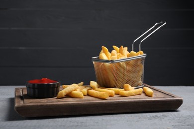 Photo of Tasty French fries served with ketchup on grey wooden table