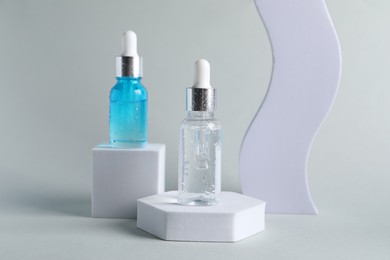 Presentation of bottles with cosmetic serums on light grey background