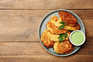 Tasty parsnip cutlets with parsley and sauce on wooden table, top view. Space for text
