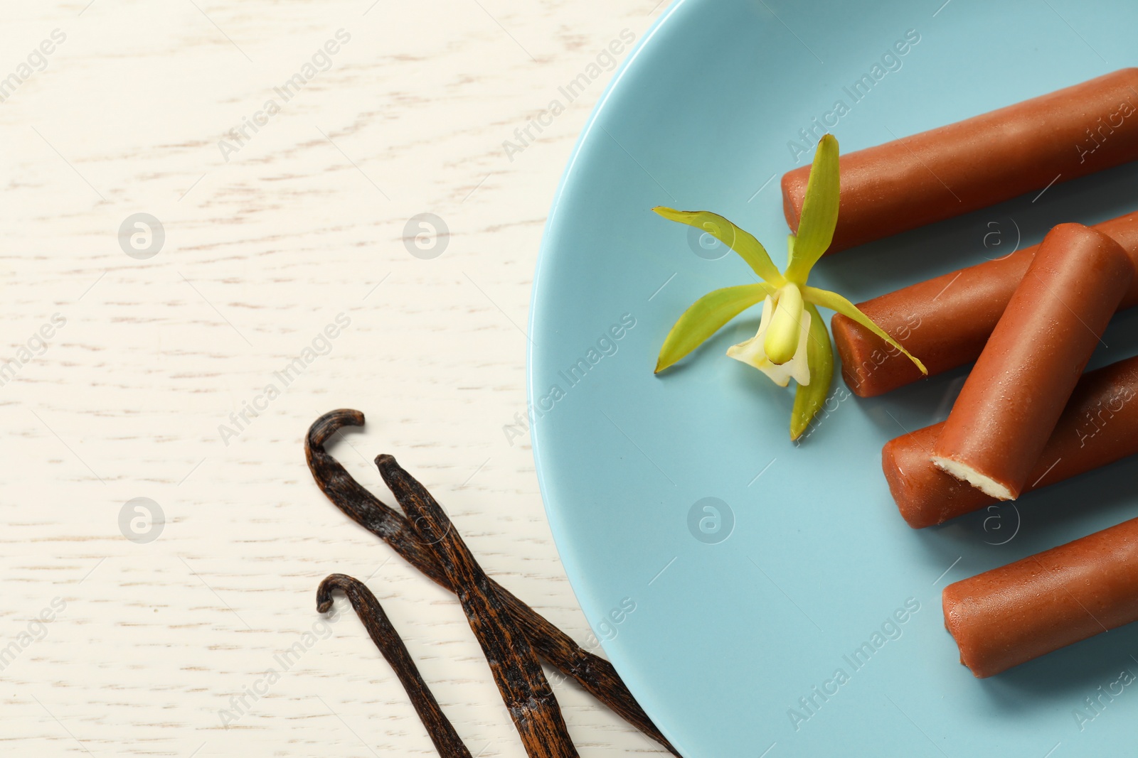 Photo of Glazed curd cheese bars, vanilla pods and flower on white wooden table, top view. Space for text