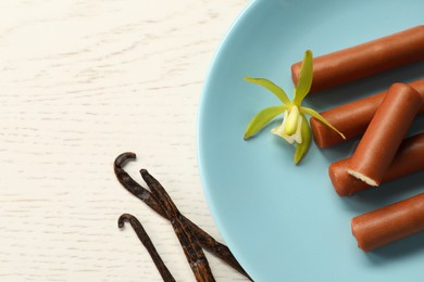 Photo of Glazed curd cheese bars, vanilla pods and flower on white wooden table, top view. Space for text