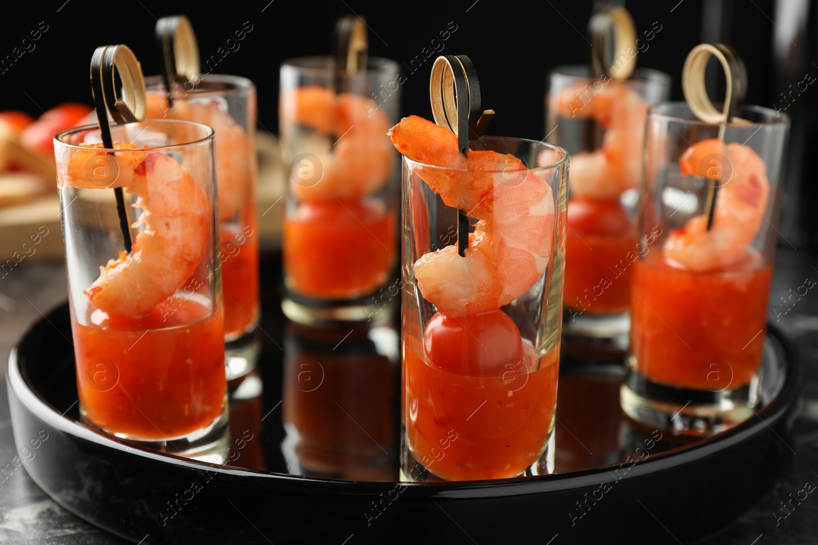 Photo of Tasty canapes with shrimps, tomatoes and sauce in shot glasses on black table, closeup