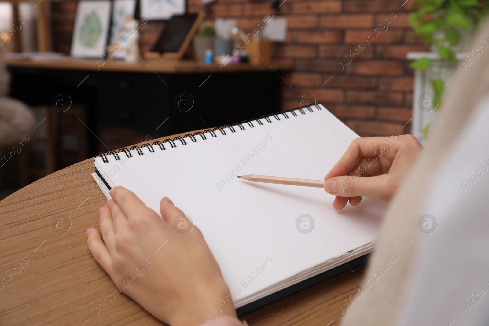 Photo of Woman drawing in sketchbook with pencil at home, closeup