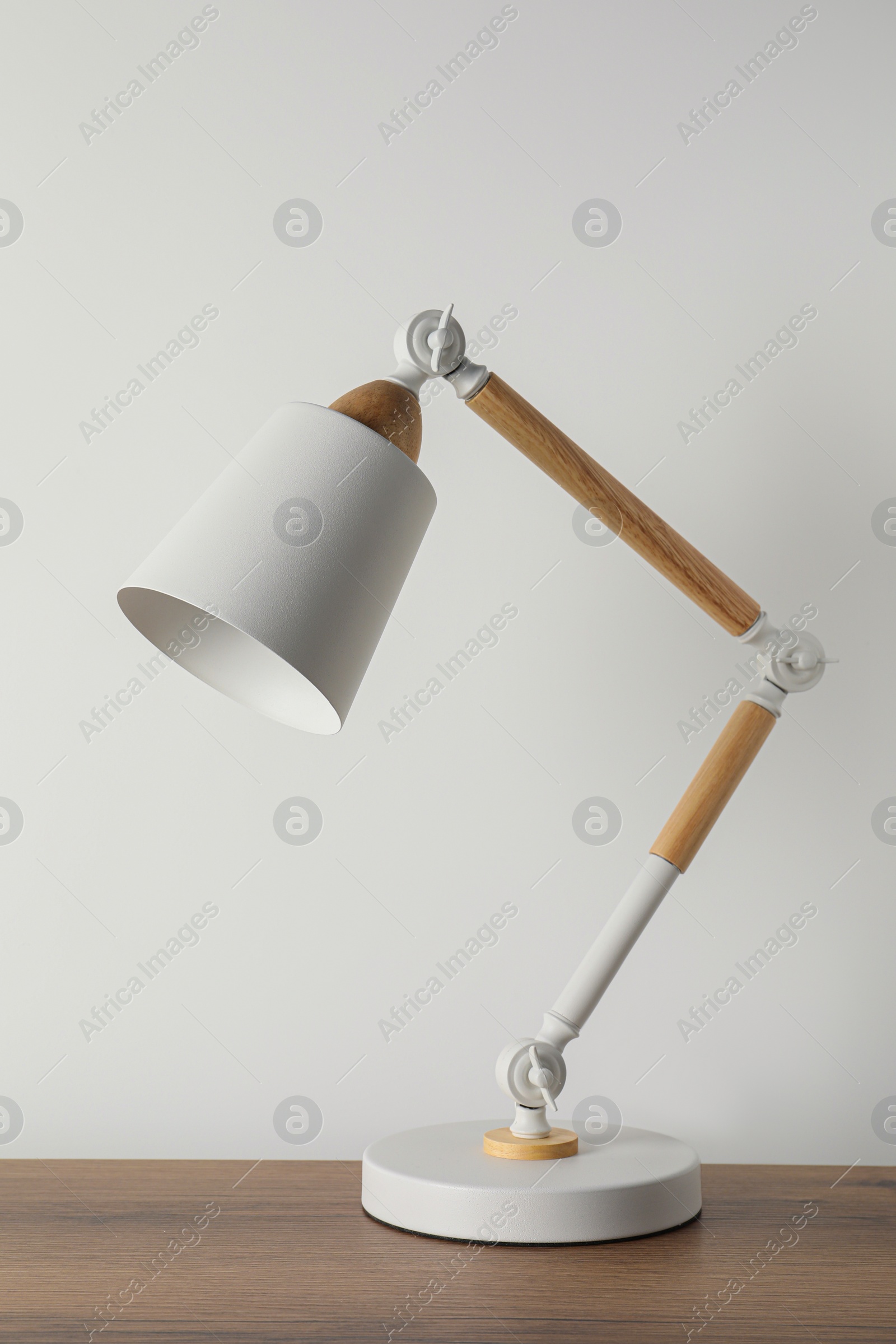 Photo of Stylish modern desk lamp on wooden table near white wall