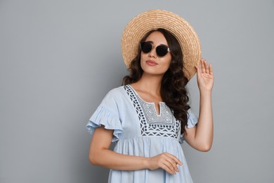 Beautiful young woman with straw hat and stylish sunglasses on light grey background