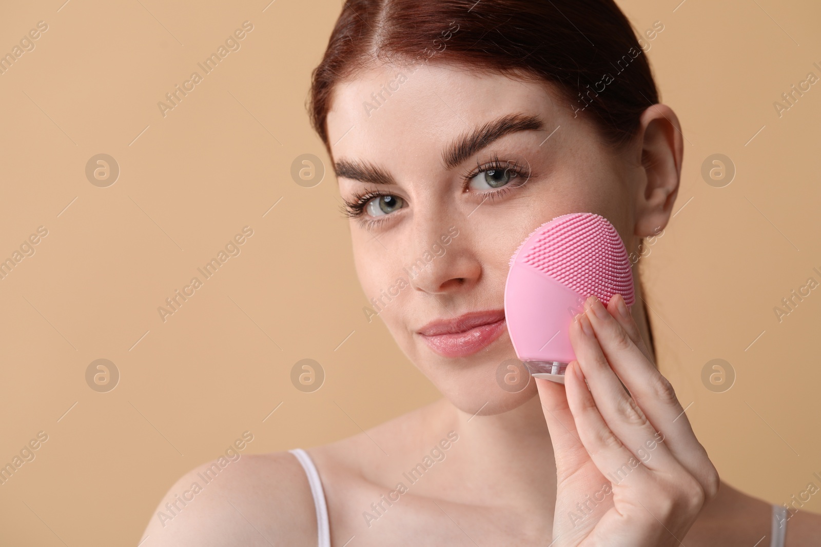 Photo of Washing face. Young woman with cleansing brush on beige background, space for text