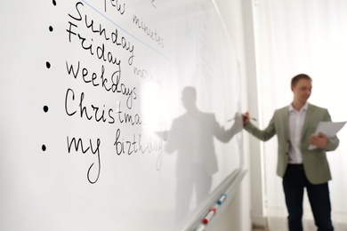 Photo of English teacher giving grammar lesson in classroom, focus on whiteboard