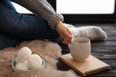 Photo of Woman in warm socks relaxing with cup of hot winter drink near window. Cozy season