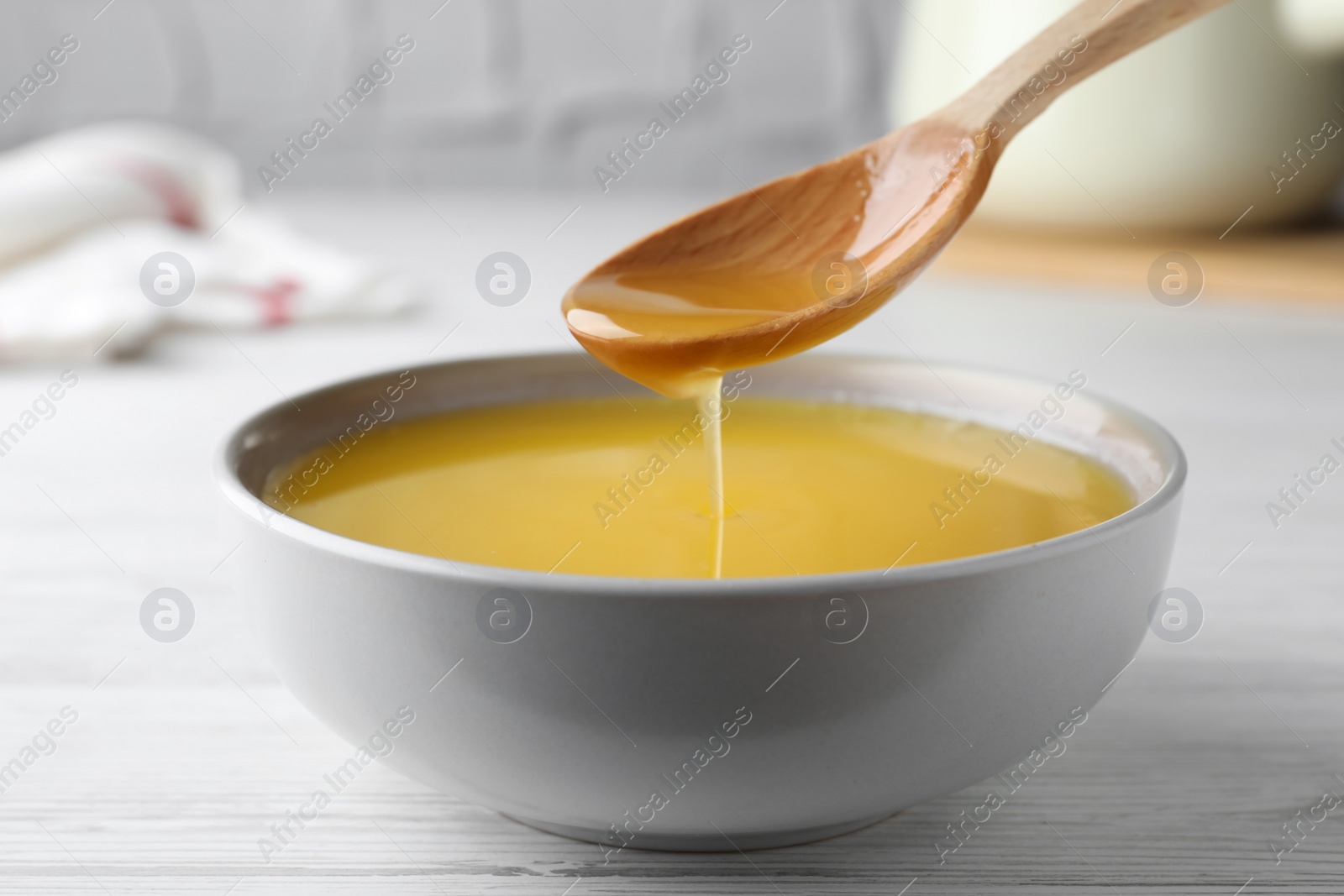 Photo of Spoon of clarified butter over bowl on white wooden table