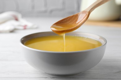 Spoon of clarified butter over bowl on white wooden table