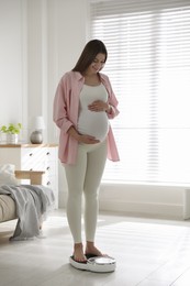 Pregnant woman standing on scales at home