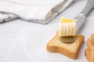 Photo of Tasty butter curls, knife and pieces of dry bread on white tiled table, closeup. Space for text