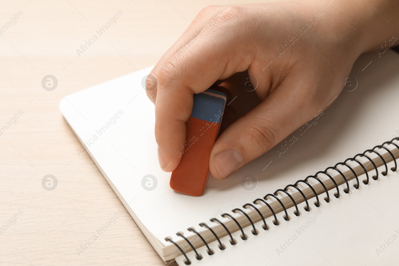 Photo of Man erasing something in notebook at wooden table, closeup
