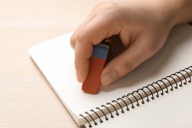 Photo of Man erasing something in notebook at wooden table, closeup