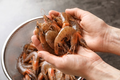 Photo of Woman holding fresh shrimps over colander, closeup