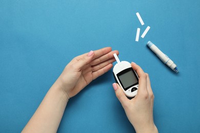 Diabetes. Woman checking blood sugar level with glucometer on blue background, top view