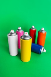 Photo of Colorful cans of spray paints on green background