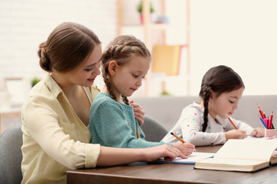 Mother helping her daughters with homework at table indoors