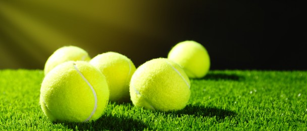 Tennis balls on green grass against dark background, space for text. Banner design