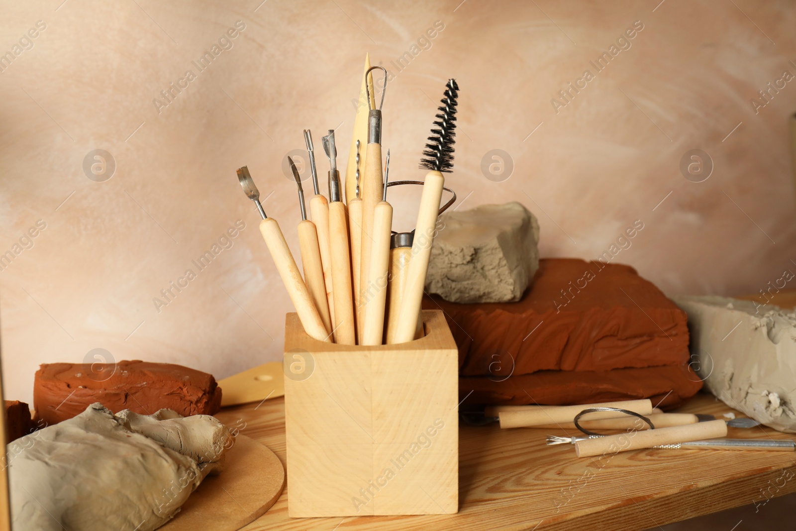 Photo of Clay and set of modeling tools on wooden table in workshop