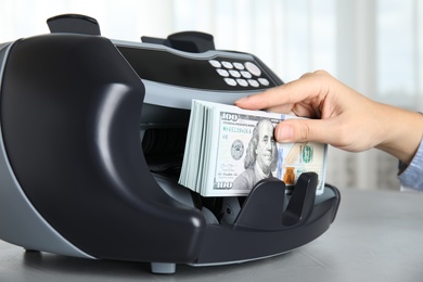 Photo of Woman taking money from counting machine at table indoors, closeup