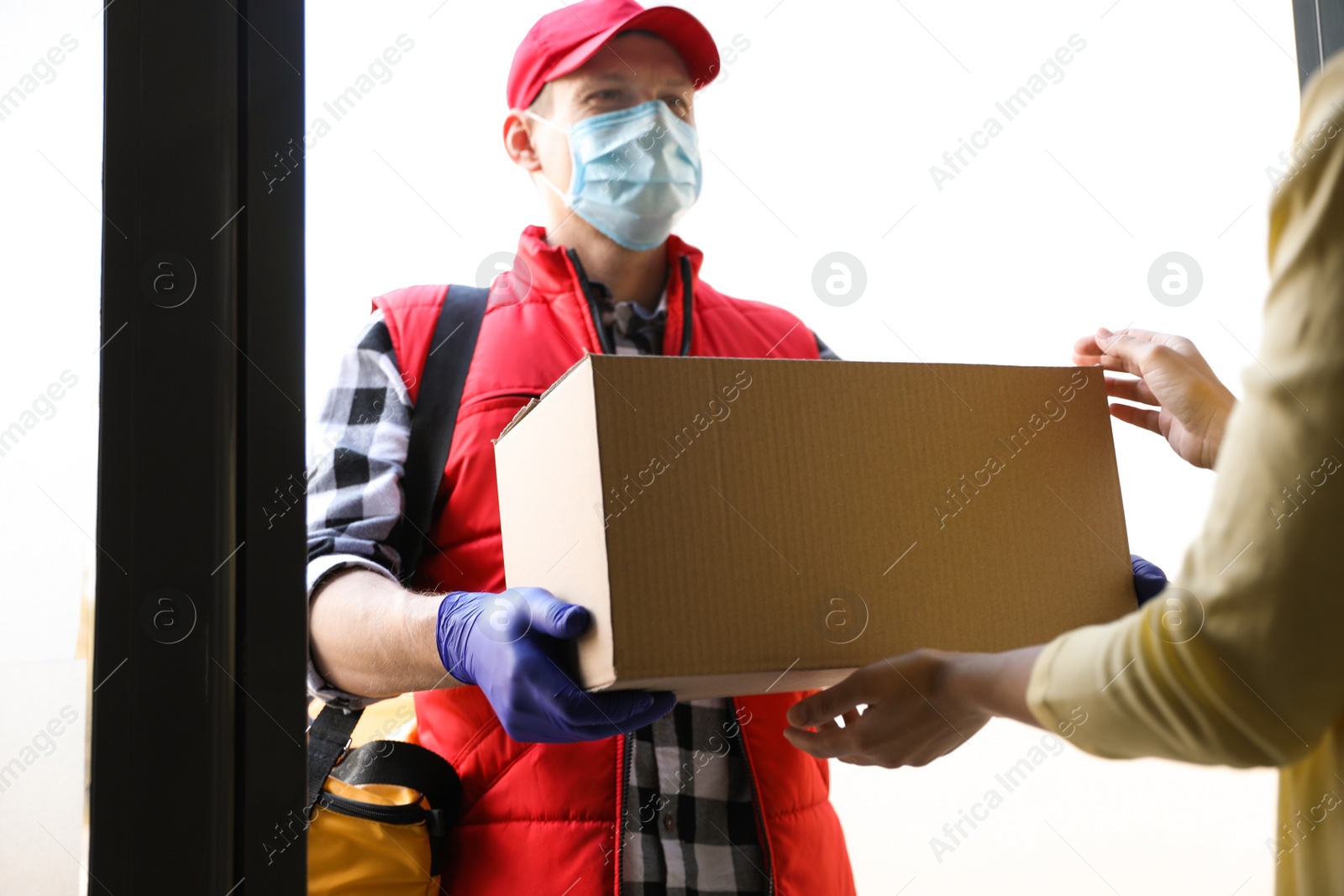 Photo of Courier giving cardboard box to woman at entrance. Delivery service during coronavirus quarantine