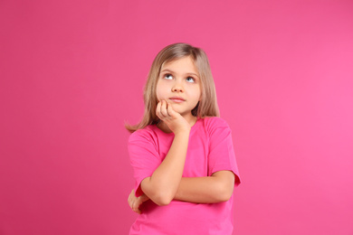 Photo of Thoughtful little girl wearing casual outfit on pink background