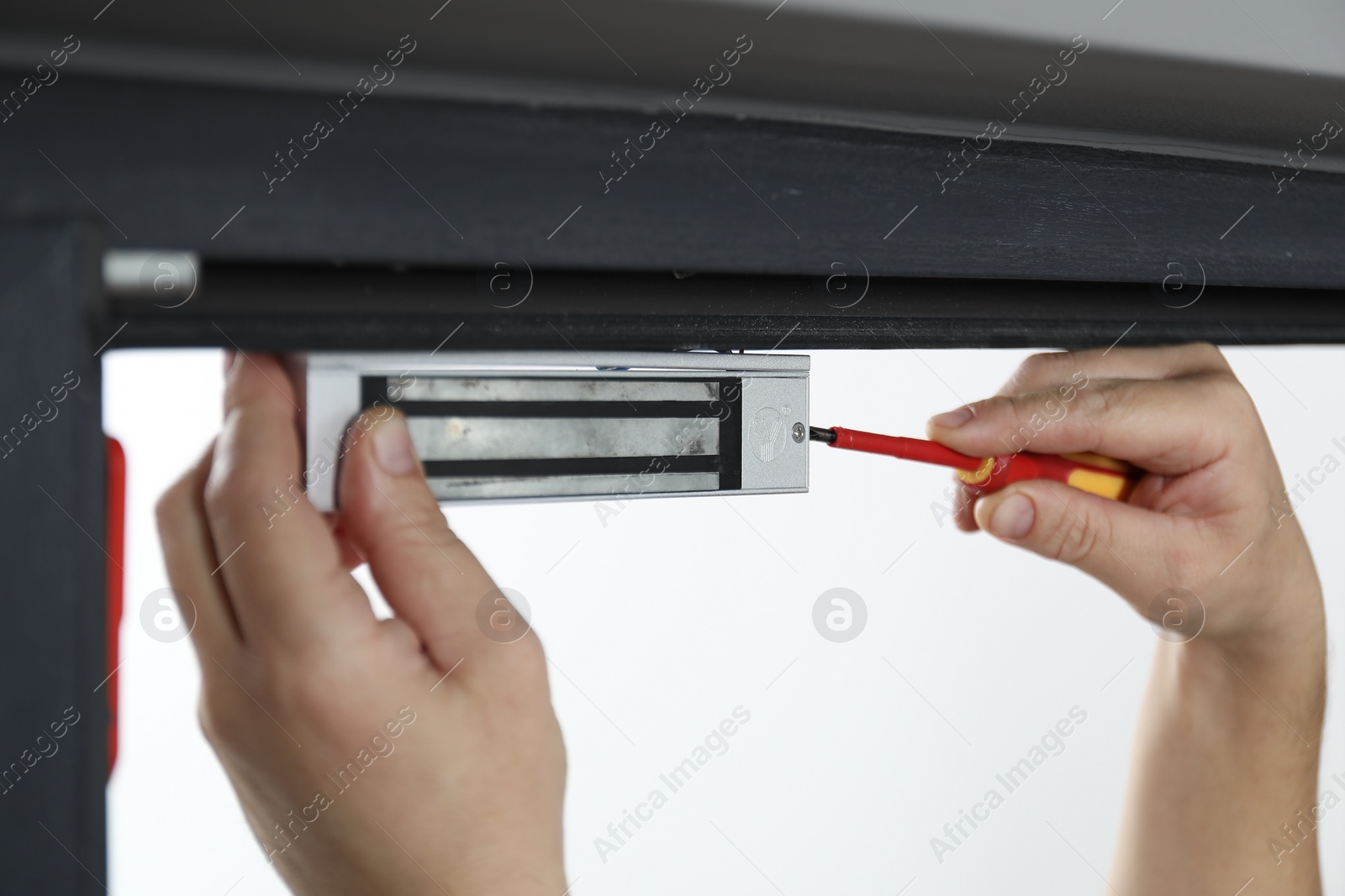 Photo of Man with screwdriver installing electromagnetic door lock indoors, closeup. Home security