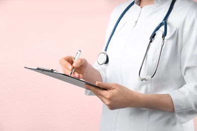 Doctor with stethoscope and clipboard on pink background, closeup. Medical service