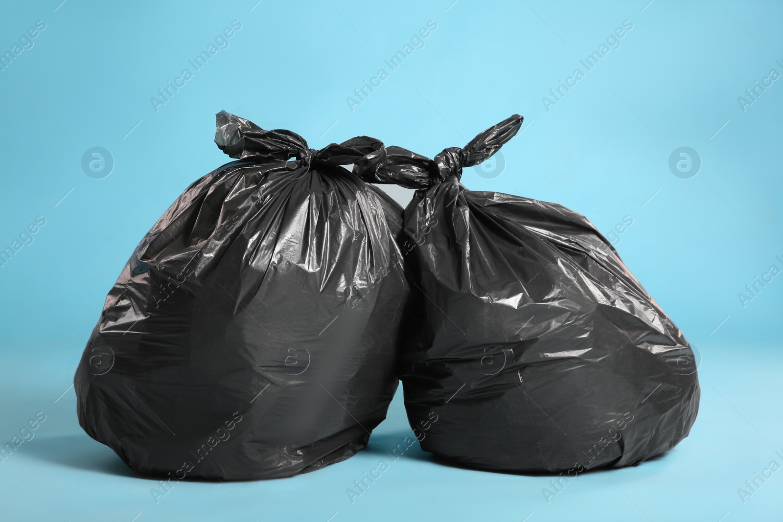 Photo of Black trash bags full of garbage on light blue background