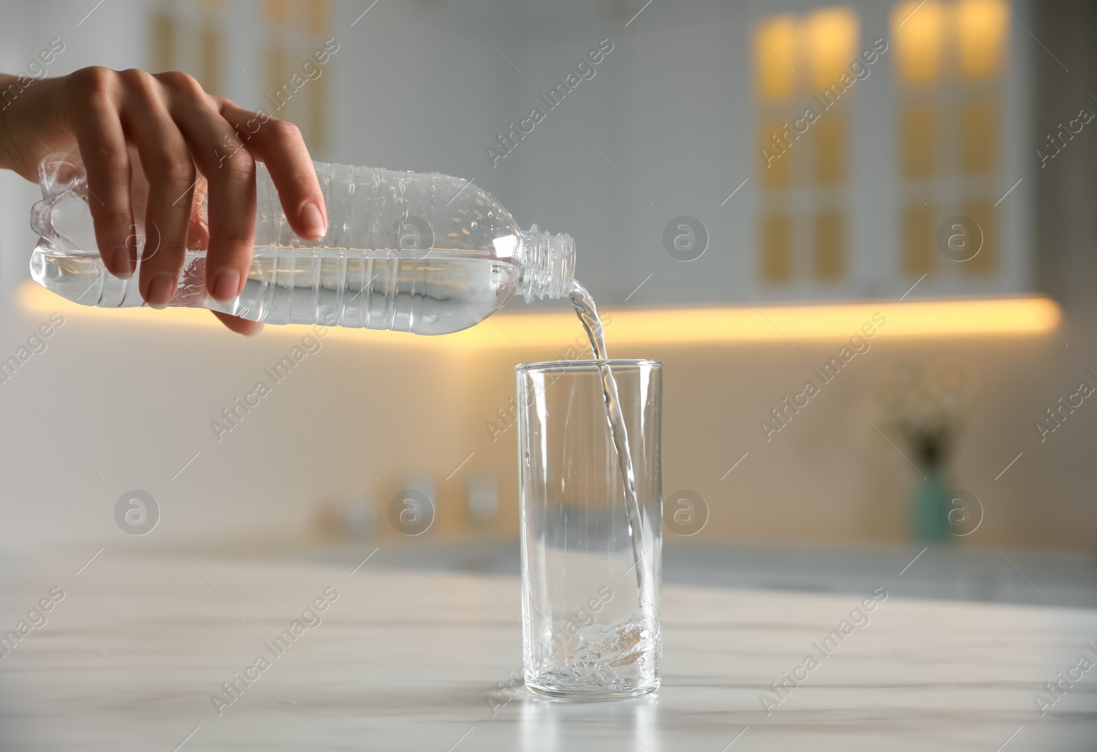 Photo of Woman pouring water from bottle into glass on table indoors, closeup