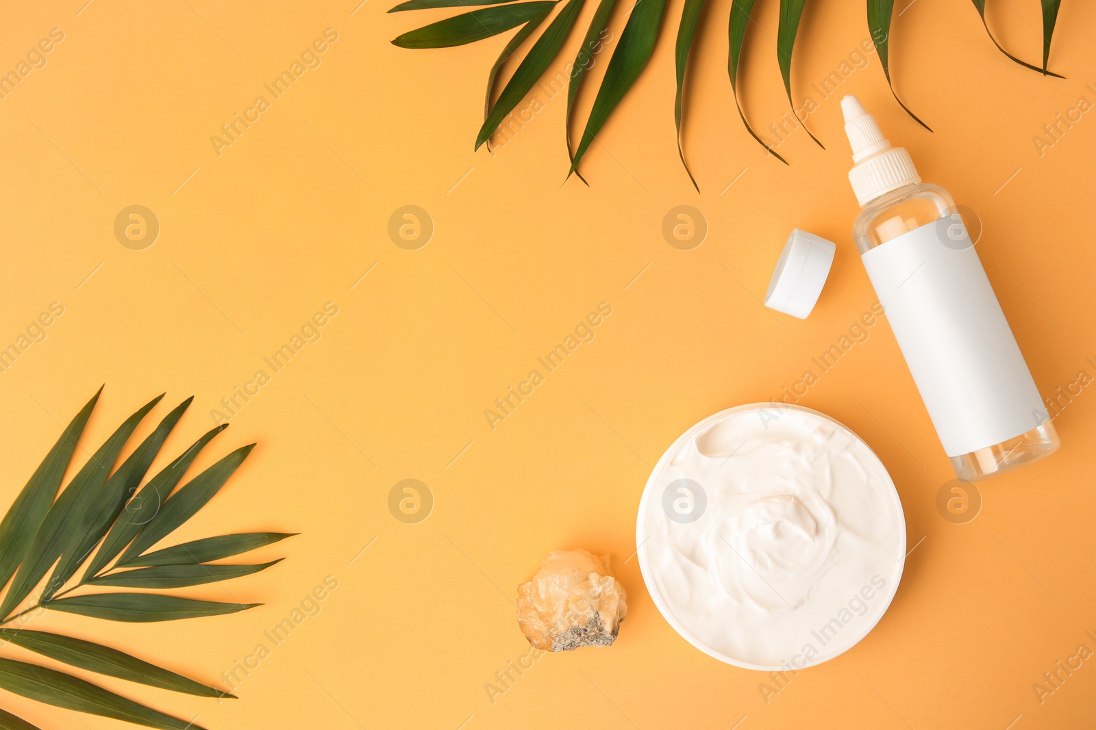 Photo of Cosmetic products, quartz gemstone and palm leaves on orange background, flat lay. Space for text