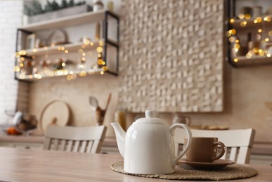Photo of White teapot with cup on wooden table in kitchen, space for text