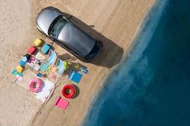 Car and beach accessories on sand near river, aerial view. Summer trip