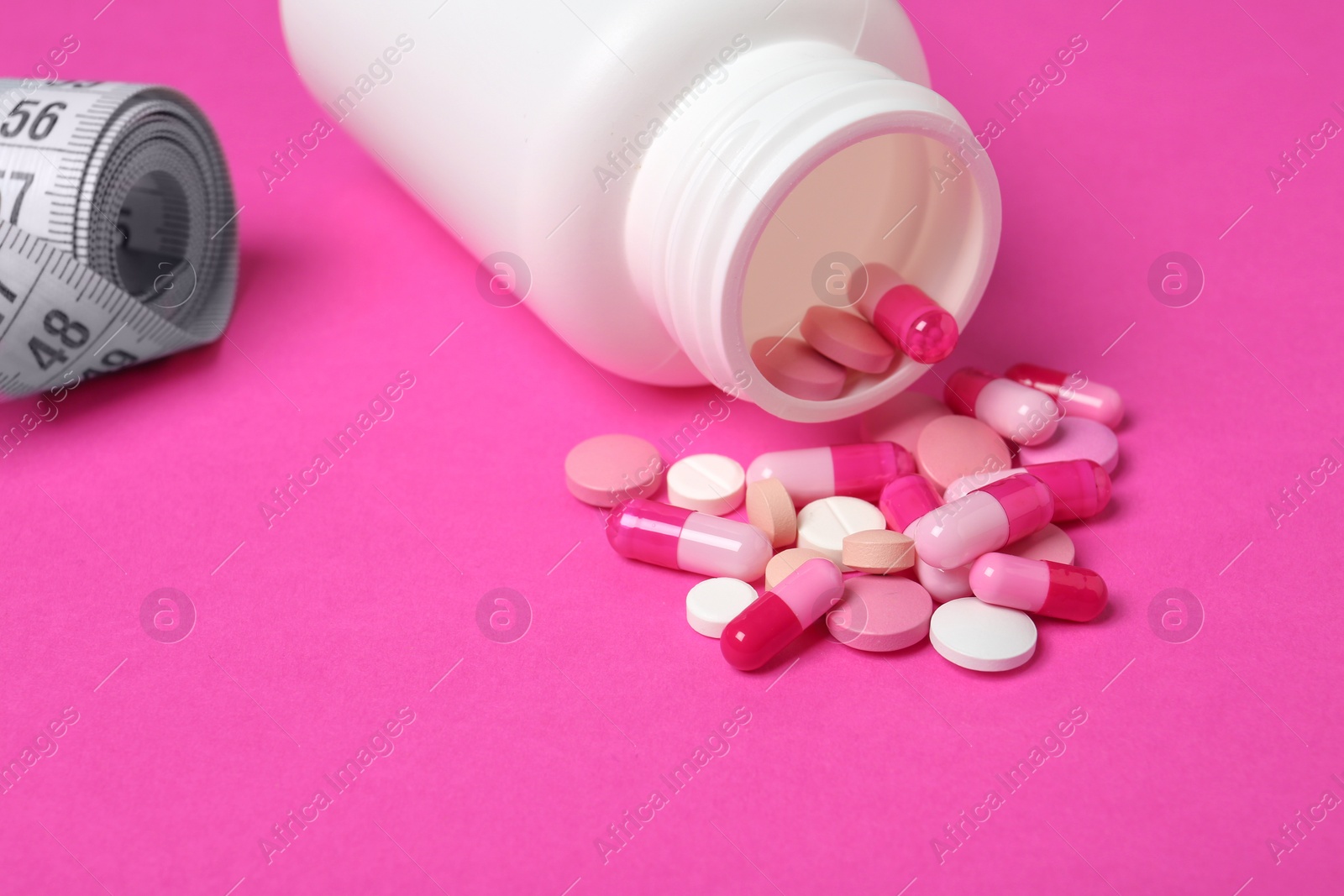 Photo of Weight loss pills, bottle and measuring tape on color background